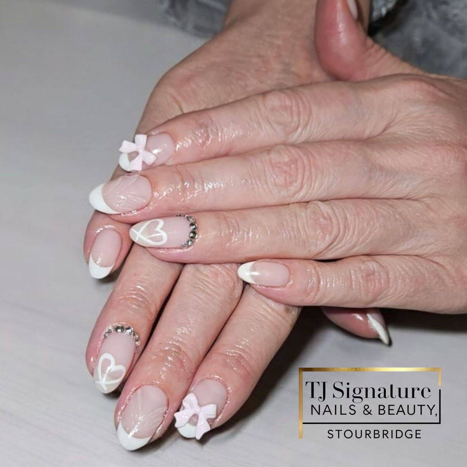 These nails feature French tips, white heart designs, pink bows, and rhinestones for a sweet, elegant look. 