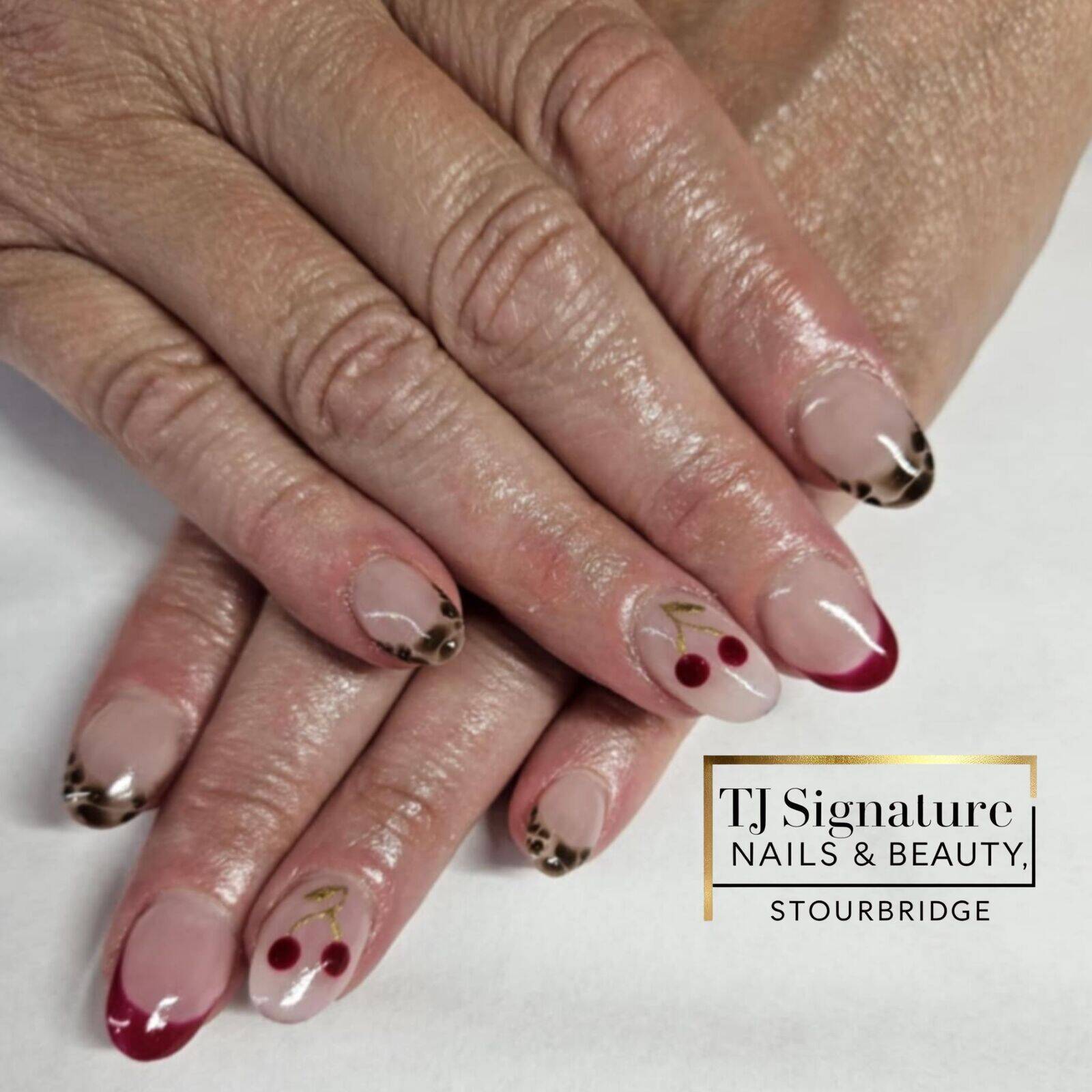 These nails mix playful and fierce — with glossy deep red cherries, bold red tips, and chic leopard print French accents on a soft nude base for a fun, fashion-forward look.